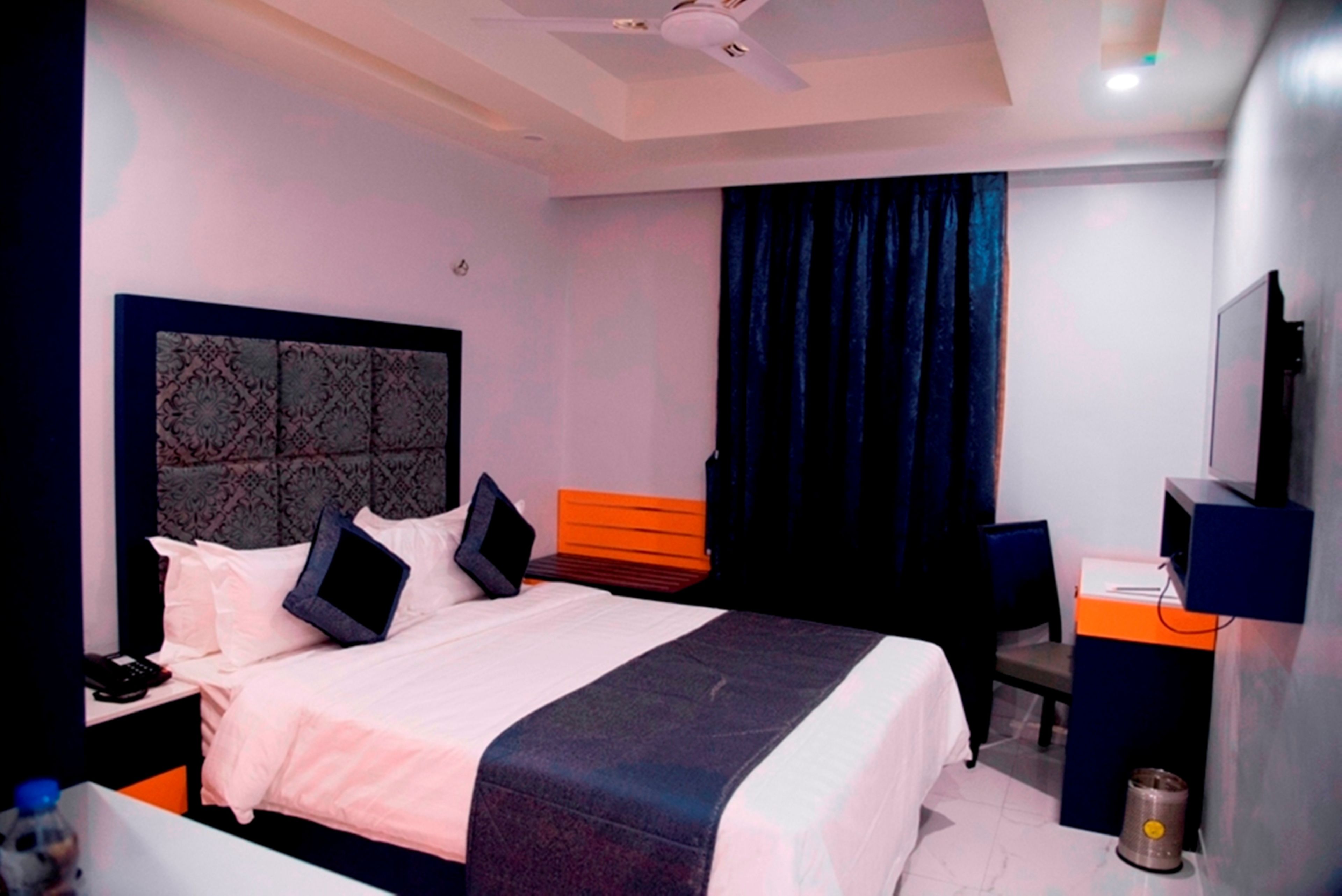 A hotel room with a bed, a desk, a chair, a television, and a ceiling fan.
