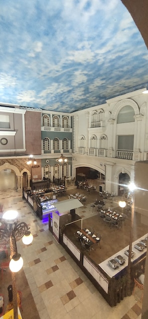 Un vaste espace intérieur comprenant plusieurs tables et chaises, un présentoir central et une fresque murale au plafond.