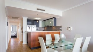 A modern kitchen with a central island, white chairs around a glass table, and a visible microwave. - Nautilus by Rockingham Apartments (Rockingham)
