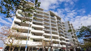 A multi-story building with balconies, a storefront, and a parked car. - Nautilus by Rockingham Apartments (Rockingham)