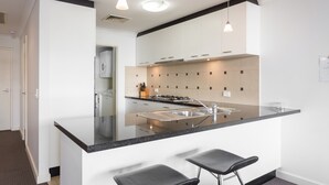A modern kitchen with a central island, bar stools, and pendant lighting. - Nautilus by Rockingham Apartments (Rockingham)