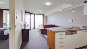 A modern hotel room with a kitchenette, a sofa, a dining area, and a large window offering a view. - Nautilus by Rockingham Apartments (Rockingham)