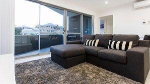 Ein modernes Wohnzimmer mit einer Eckcouch, einer großen Schiebeglastür, die auf einen Balkon führt, und einem Teppichboden.