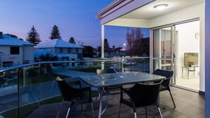 Ein moderner Essbereich im Freien mit einem Glastisch und Stühlen, mit Blick auf einen Pool und benachbarte Häuser.