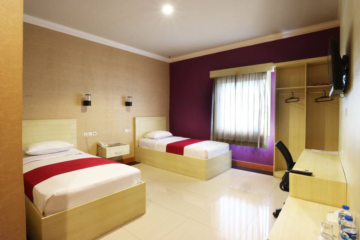 A hotel room with two beds, a desk, a chair, a TV, and a wardrobe.