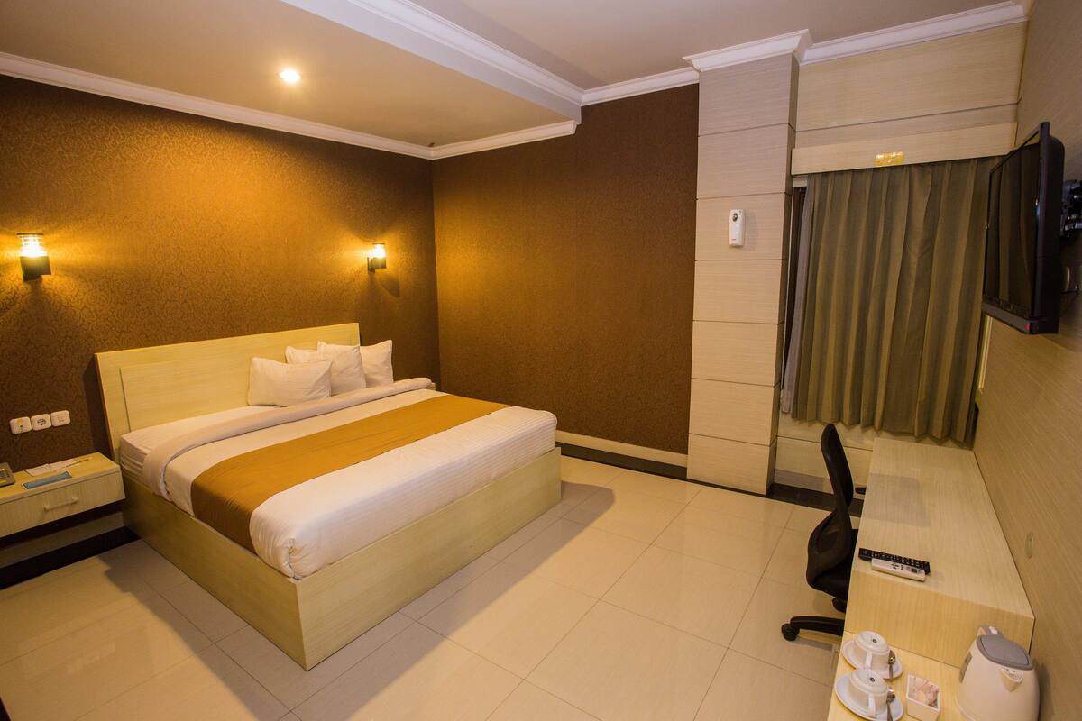 A hotel room with a large bed, bedside tables, a desk with a chair, a television, and a bathroom with a curtain.