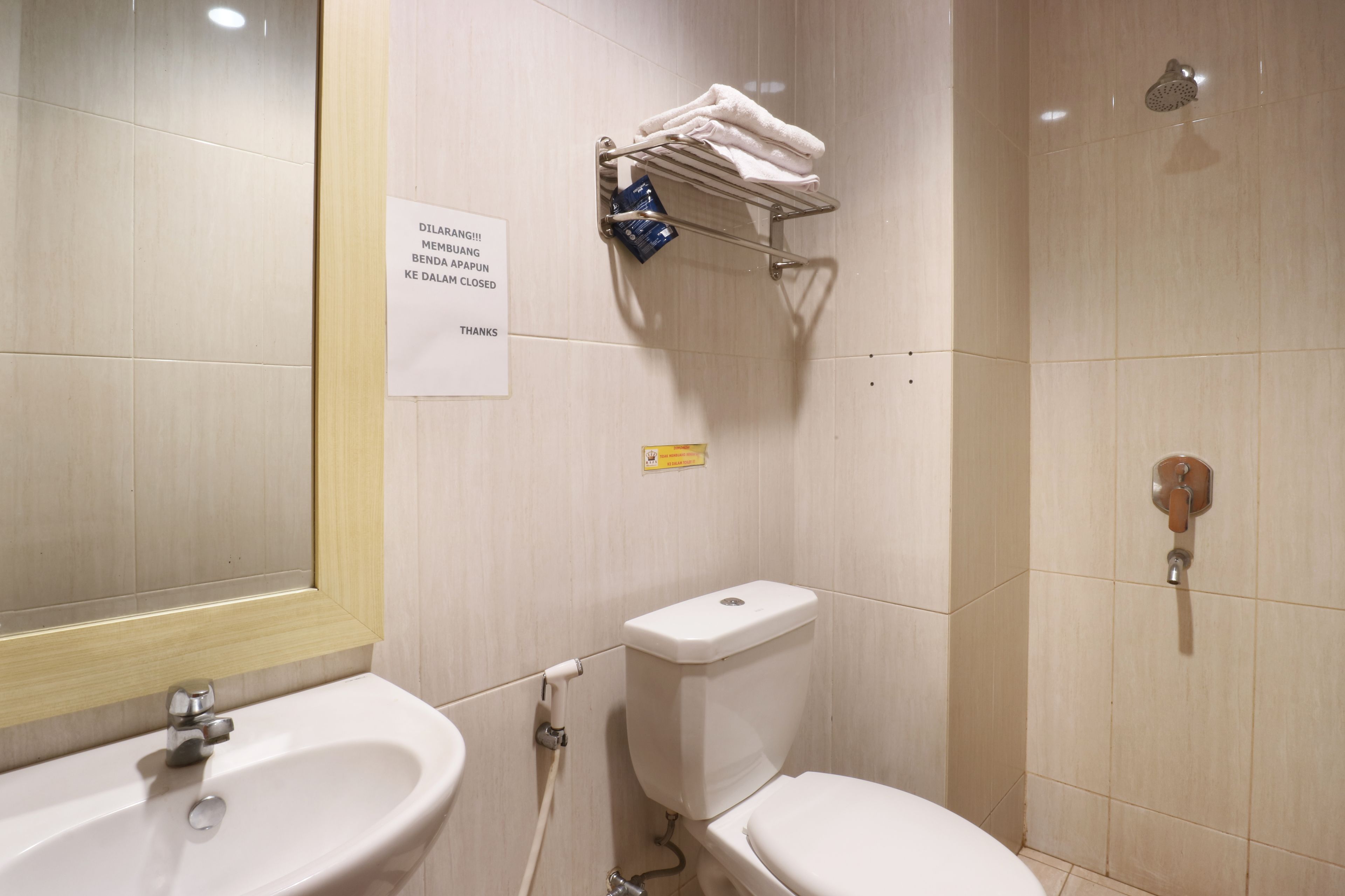 Een badkamer met een wastafel, toilet en douche. Er hangt een bord aan de muur en een handdoekrek met handdoeken.