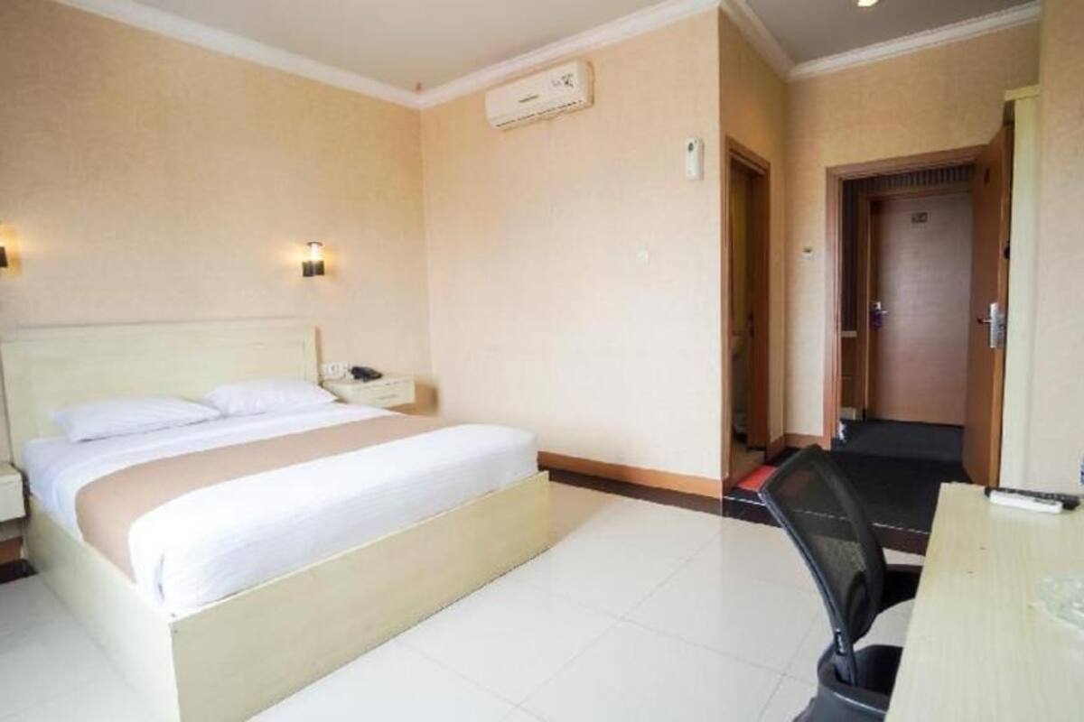 A hotel room with a bed, bedside table, lamp, and a desk with a chair.