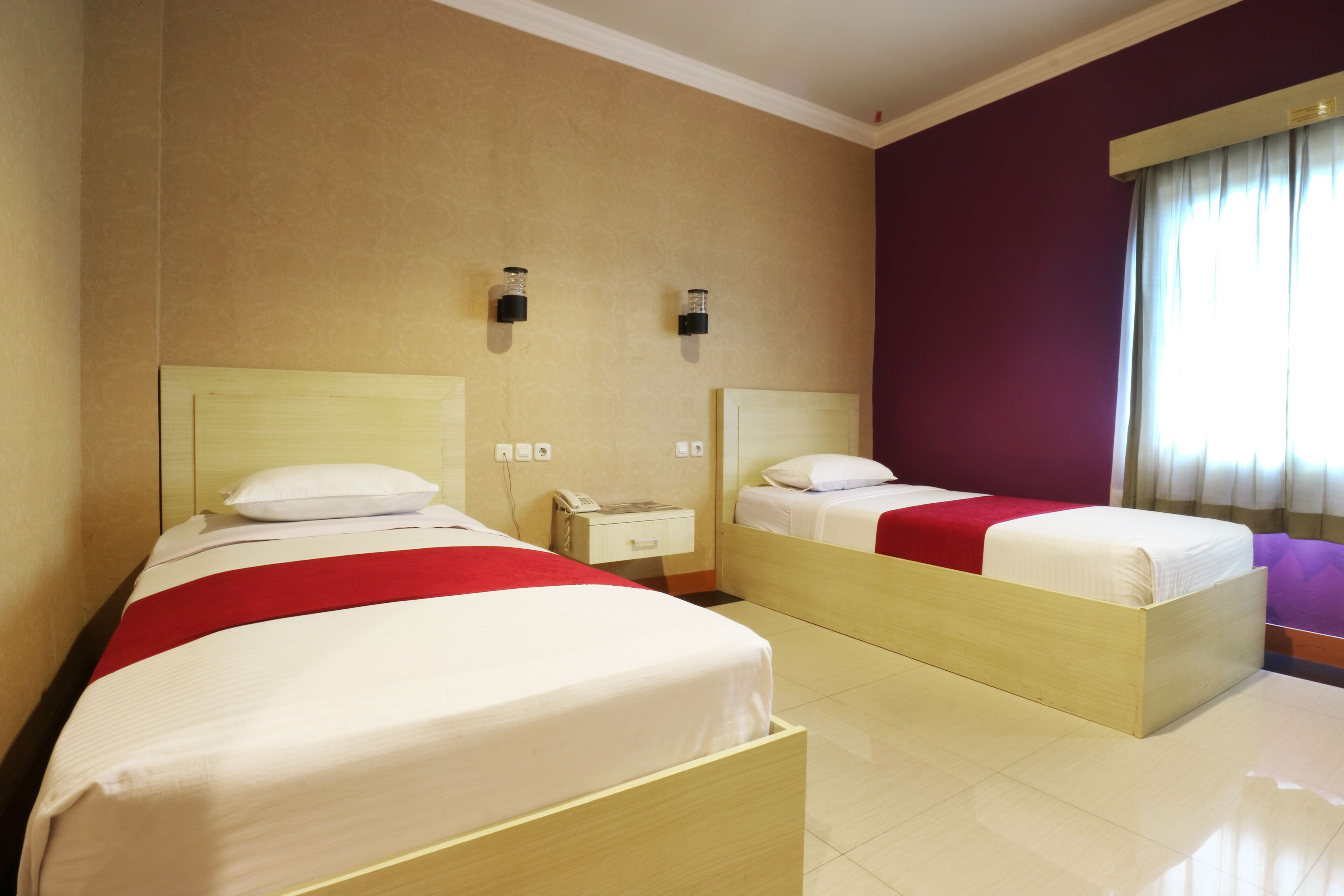 Ein Hotelzimmer mit zwei Betten, einem Nachttisch und einem Fenster mit Vorhängen.