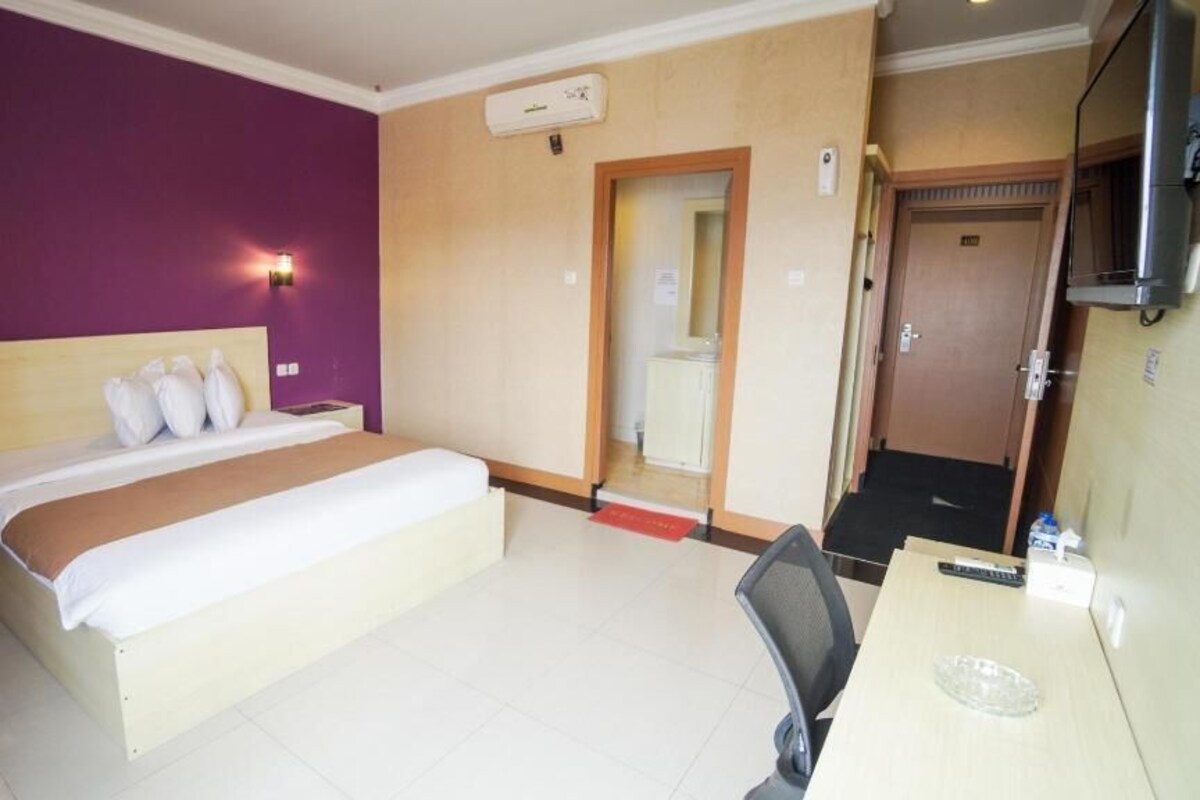 A hotel room with a bed, bedside tables, a desk, a chair, a TV, and a door.