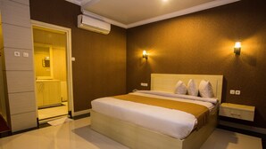 A hotel room with a large bed, a bedside table, a nightstand, a wardrobe, and an air conditioning unit. - Raja Residence (Jakarta)