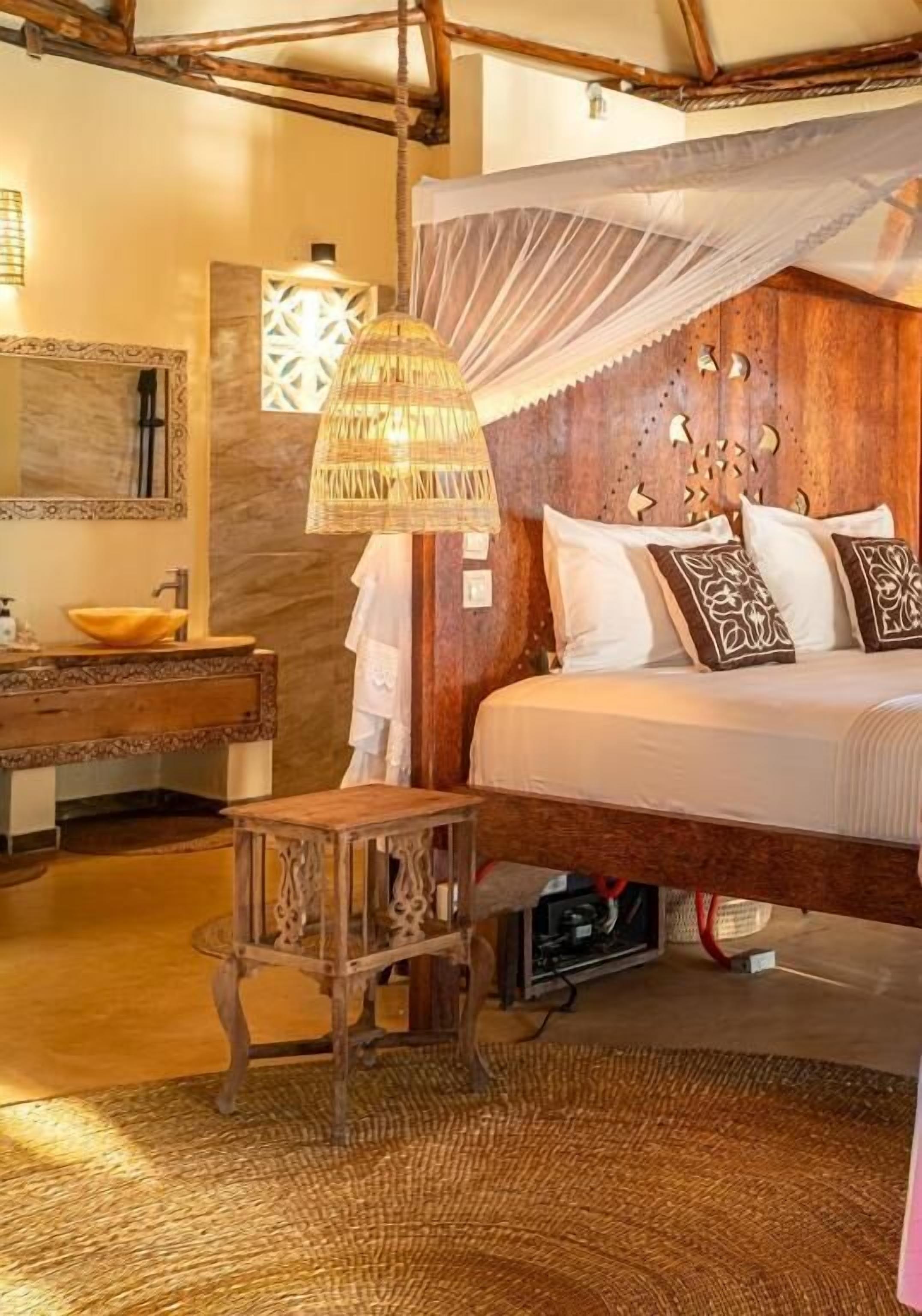 A bedroom with a wooden headboard, a canopy bed, a bedside table, a mirror, and a hanging lamp.