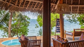 Una terraza de madera con techo de paja, bancos de madera con cojines y vista al mar.