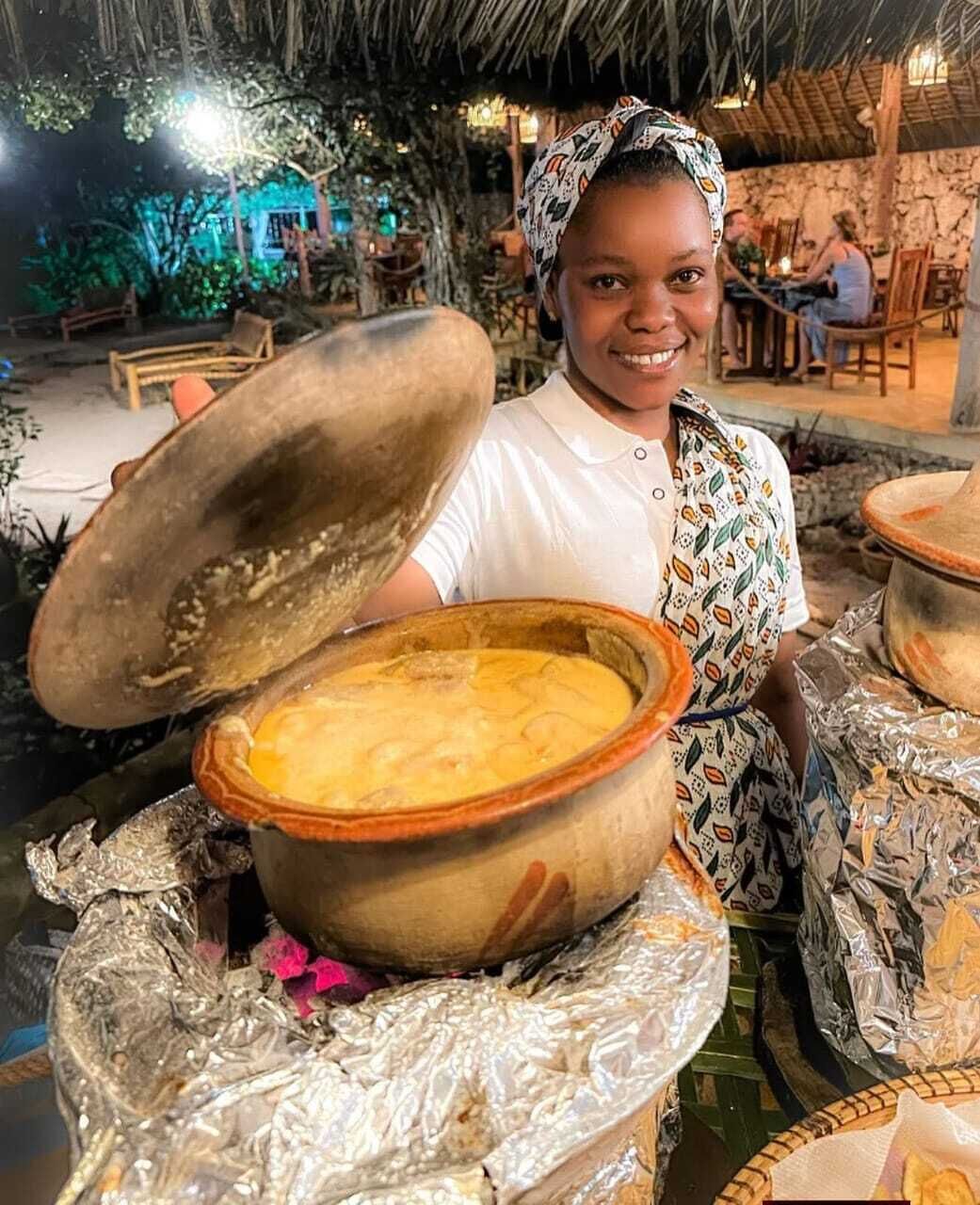 A person holding a large pot with a lid, surrounded by other pots and covered with foil.
