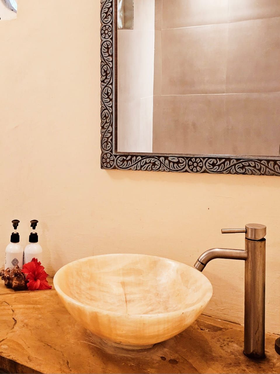 A bathroom with a wooden vanity, a vessel sink, a modern faucet, and a decorative mirror with a black frame.
