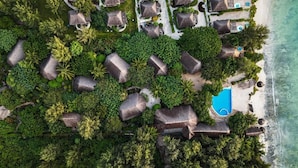 Vista aérea de un complejo turístico con cabañas de techo de paja, una piscina y una playa.