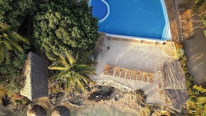 Vista aérea de un resort con piscina azul cristalina, palmeras y una zona de playa.