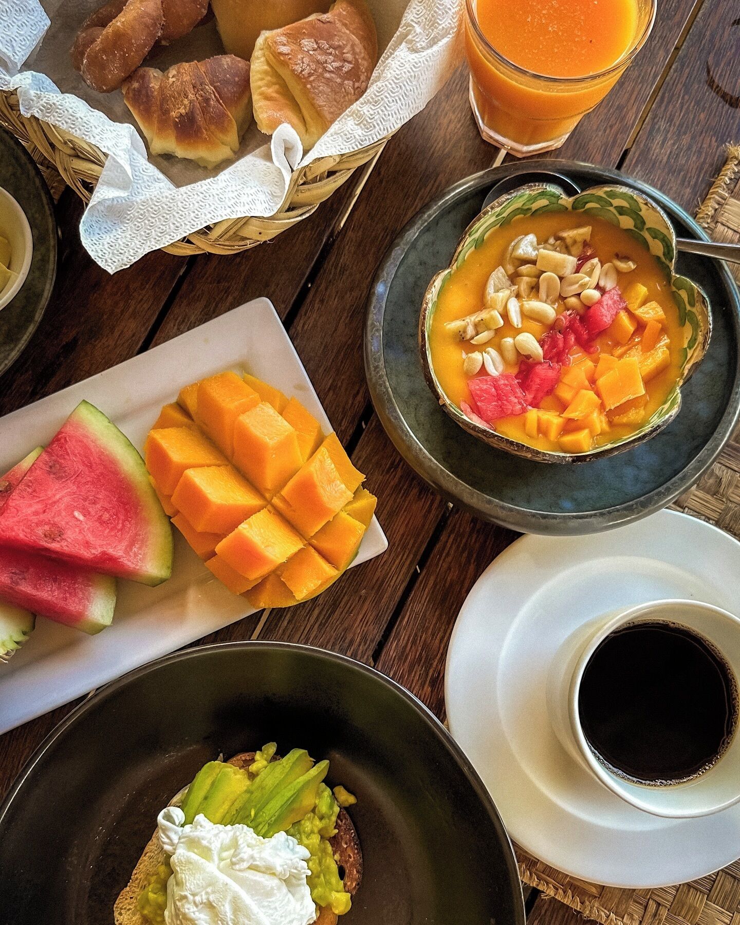 A table with various food items including bread, a bowl of soup with vegetables, mango slices, and a cup of coffee.