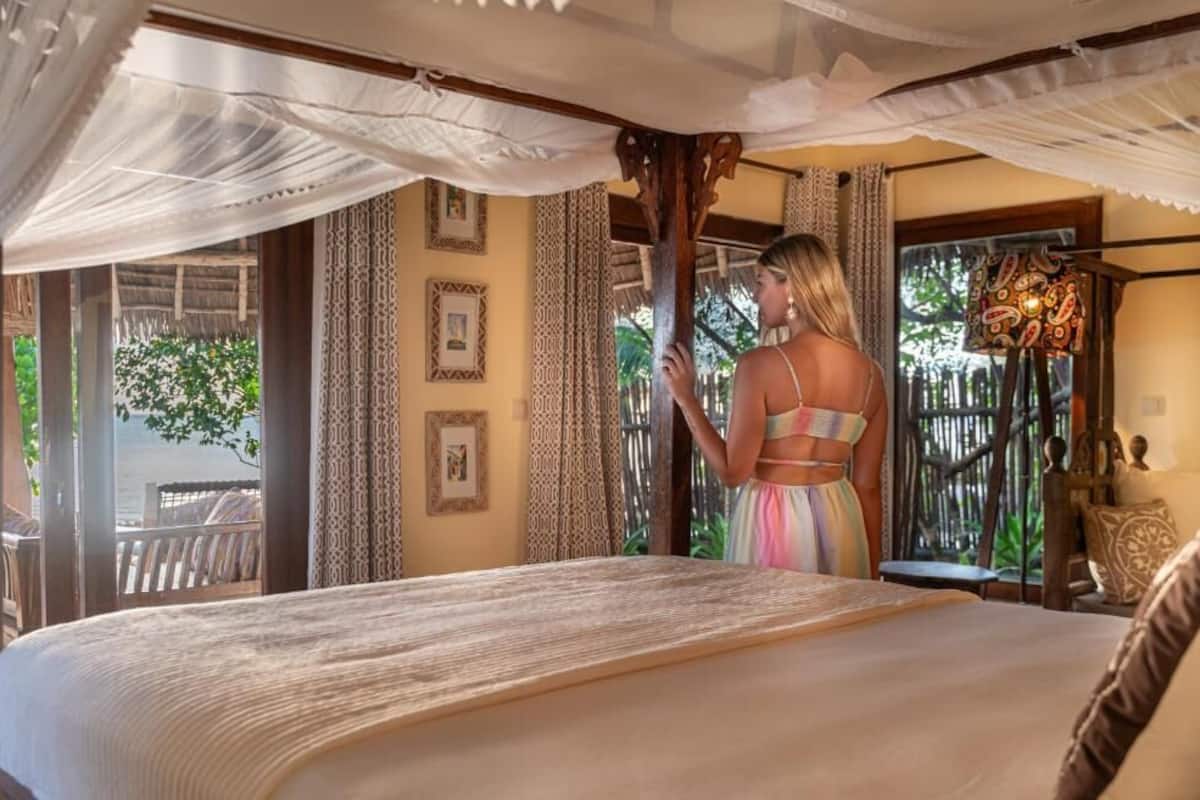 A bedroom with a bed, a canopy, a view of the outdoors, and a window with curtains.