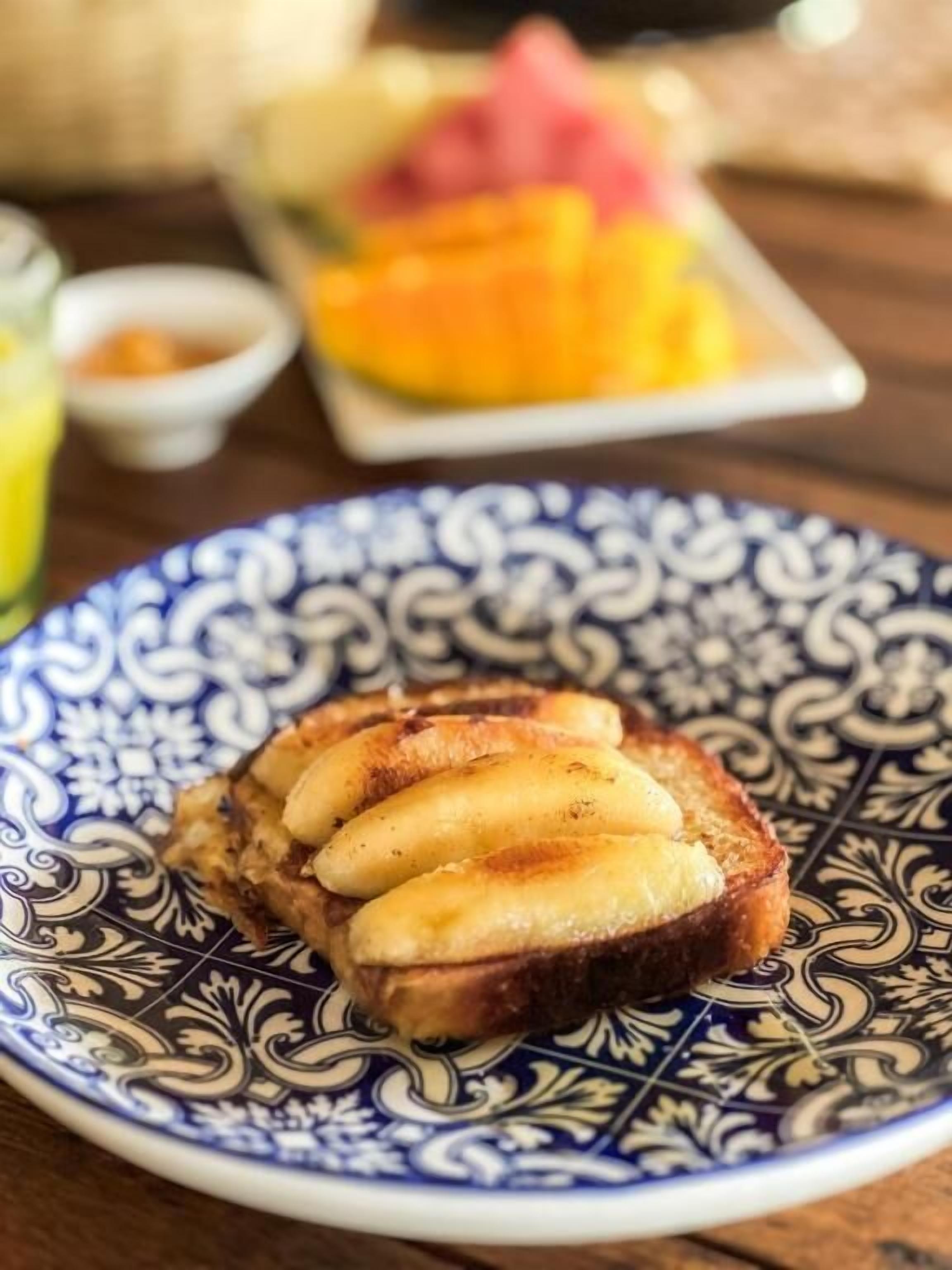 Un plato con un sándwich tostado y rodajas de plátano sobre un plato decorativo azul y blanco.