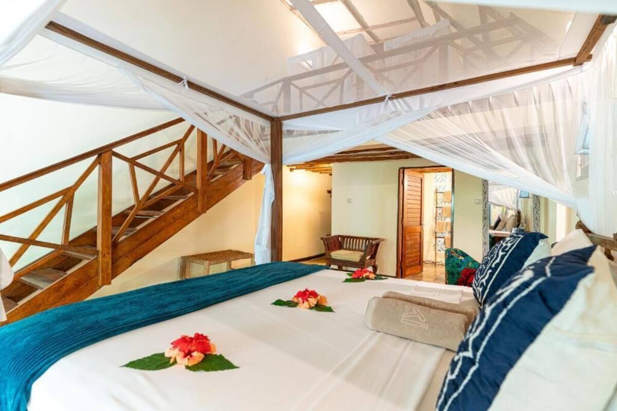 A bedroom with a bed, a chair, a staircase, and a door.