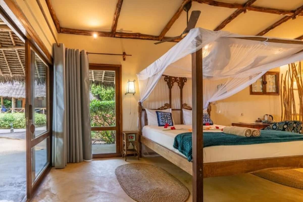 A four-poster bed with a canopy, a small bedside table, a nightstand, and a window with curtains.