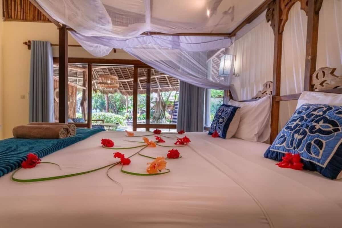 A bedroom with a canopy bed, a view of greenery outside, and a window with curtains.