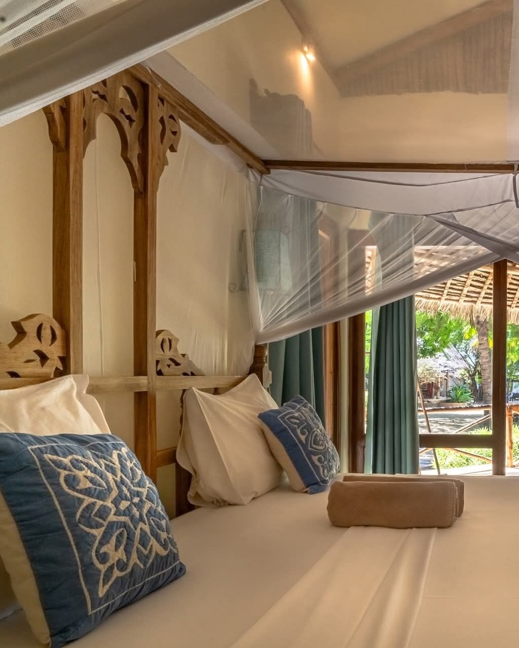 A bedroom with a canopy bed, wooden headboard, and a view of the outdoors.