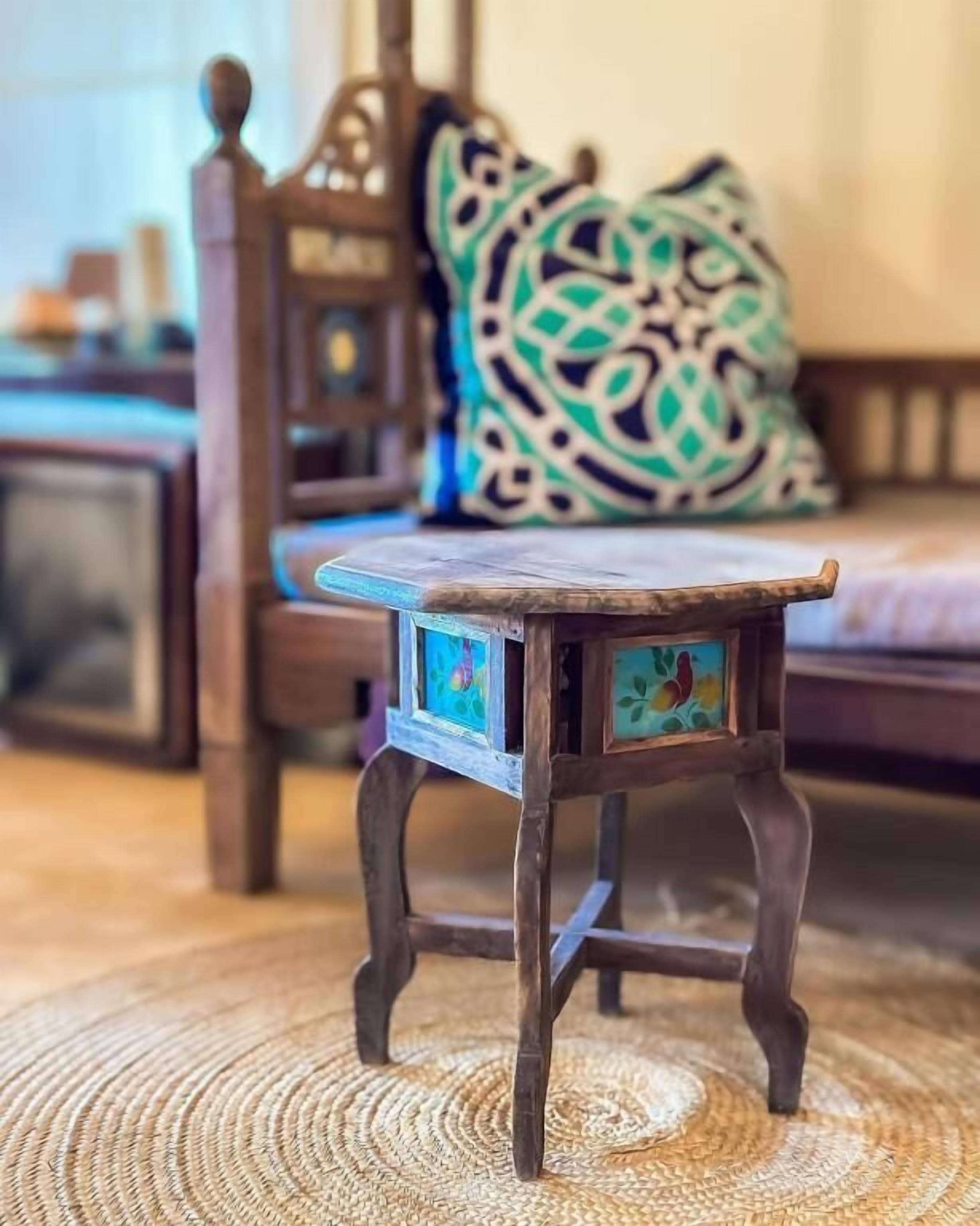 A small wooden table with a colorful inlay, placed on a woven mat.