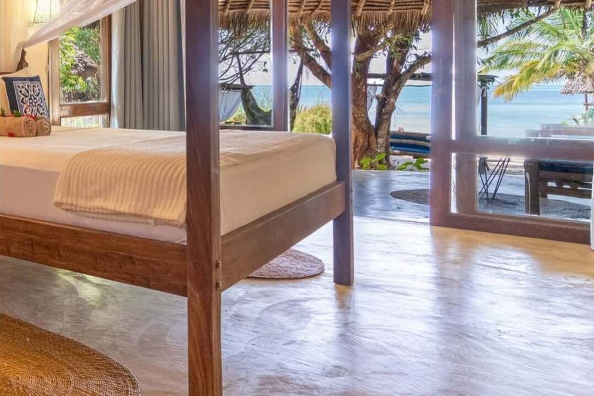A room with a four-poster bed, large windows, and a view of the beach.