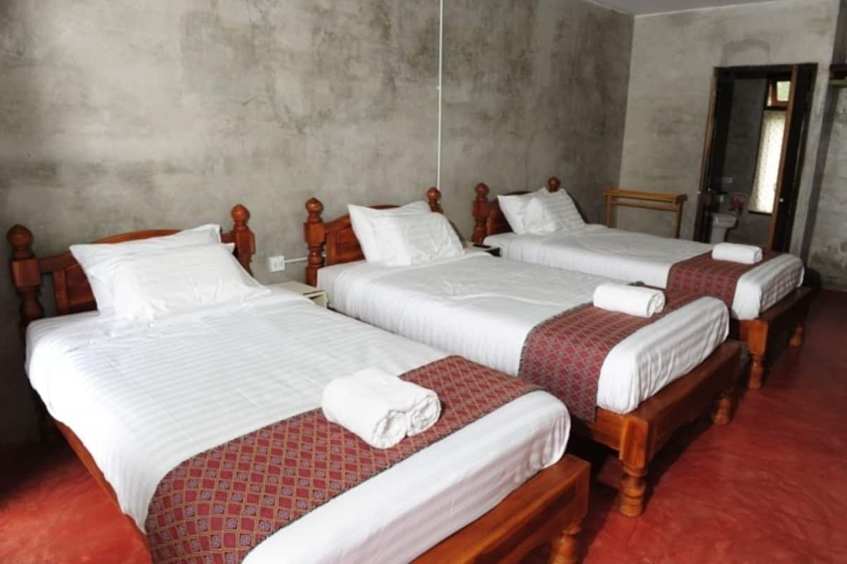 A hotel room with three wooden beds, each with white linens and red patterned bedspreads.