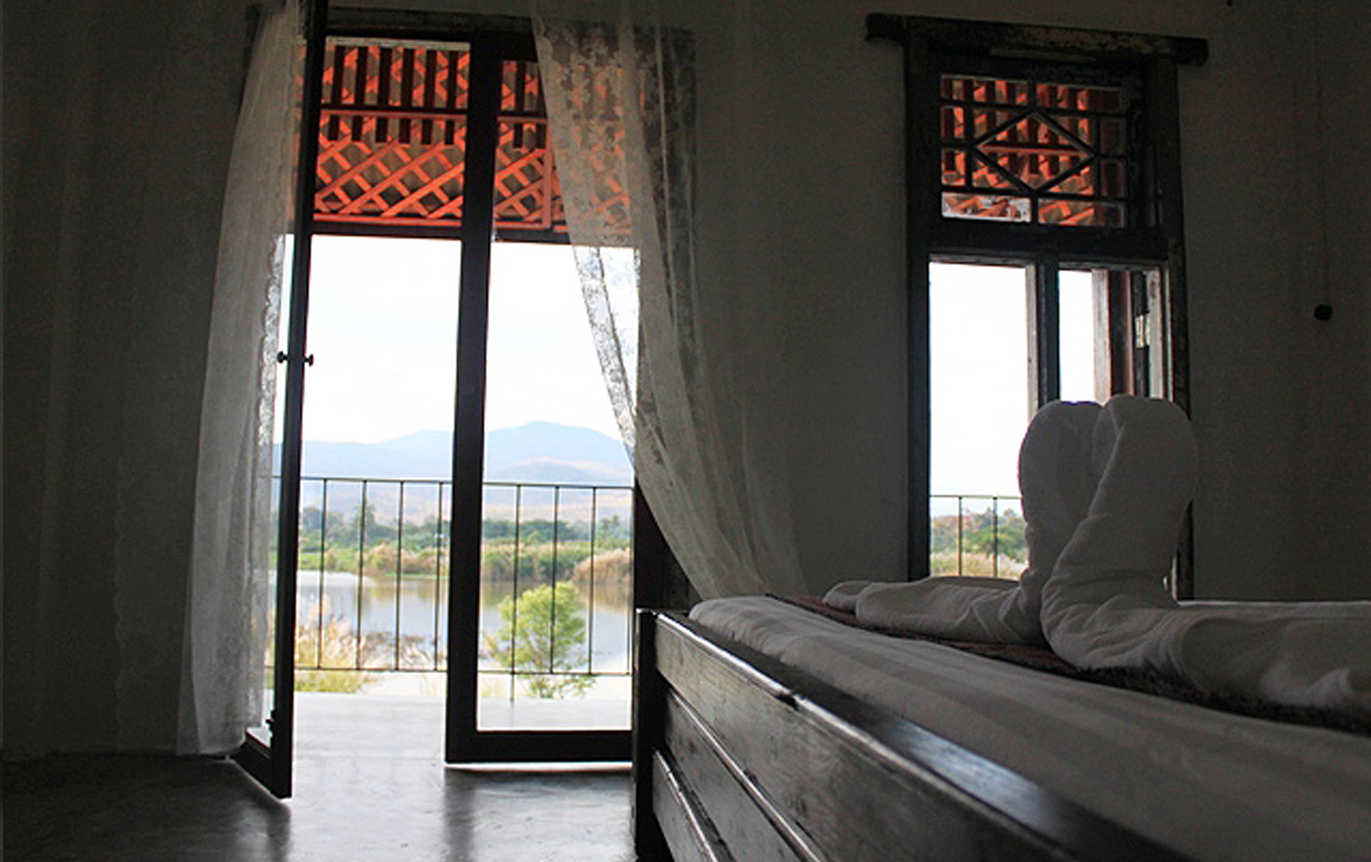 Una habitación con cama, vista a un paisaje por la ventana y un balcón con barandilla.