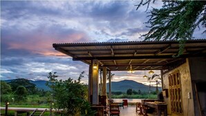 Un área de comedor al aire libre con vista a montañas, cubierta por un techo metálico y rodeada de vegetación.