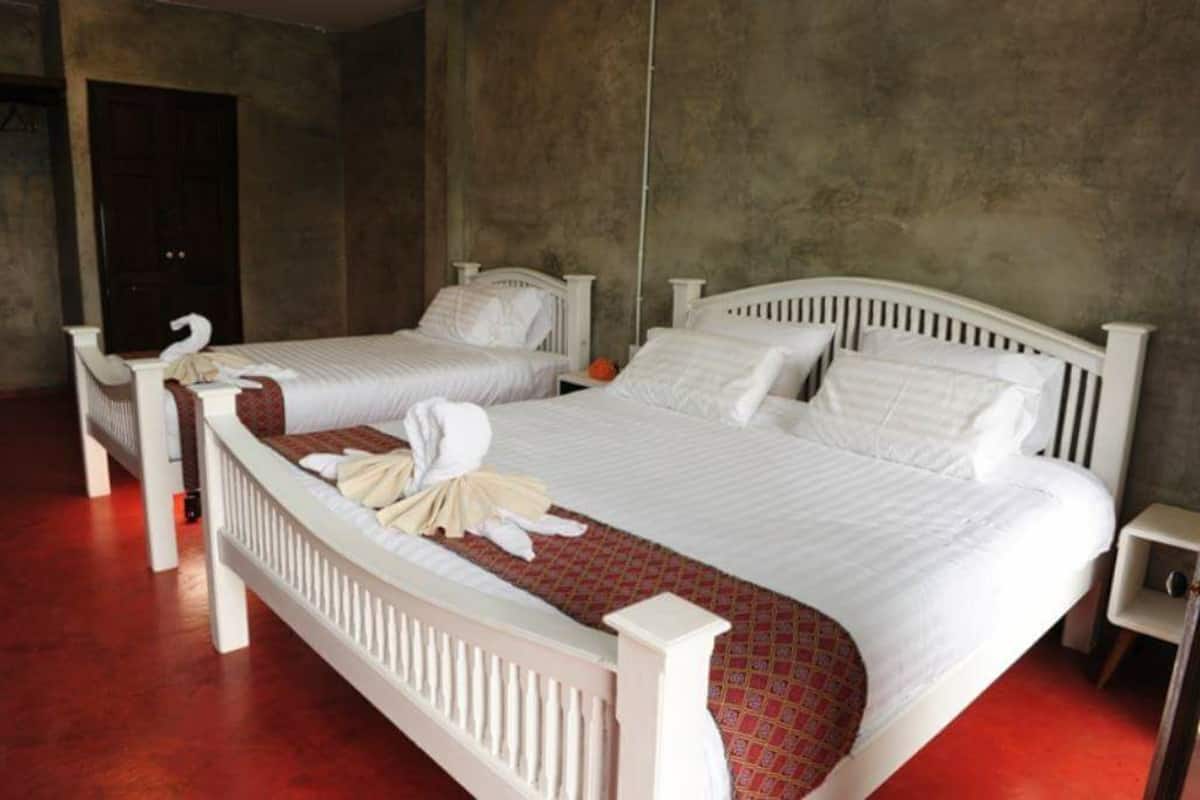 A hotel room with two single beds, a wooden headboard, a small bedside table, and a red carpeted floor.