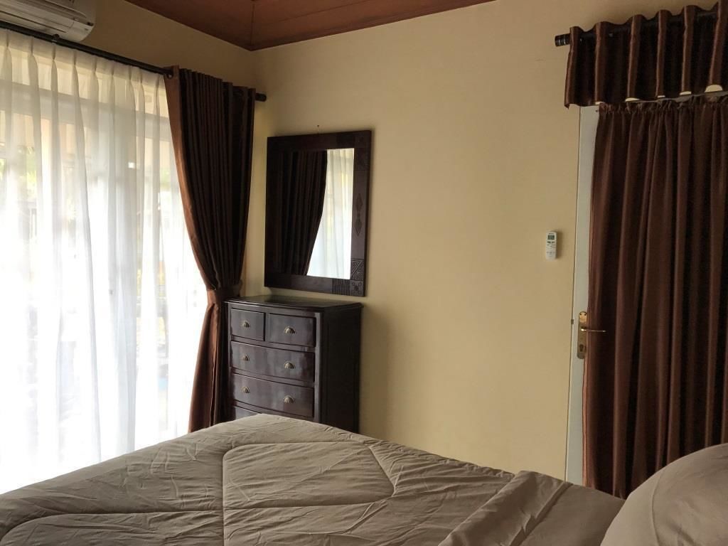 A bedroom with a bed, a dresser, a mirror, and curtains.