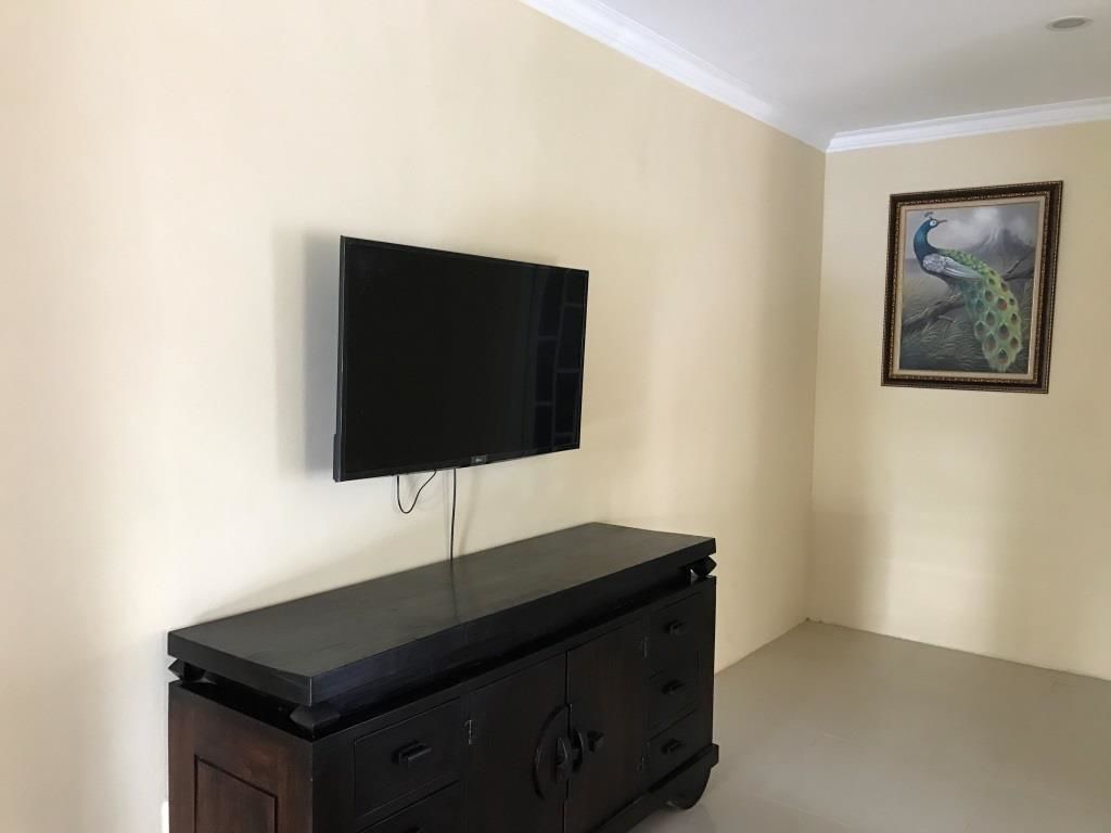 A room with a flat-screen TV mounted on the wall, a dark wooden cabinet below, and a framed peacock painting on the wall.