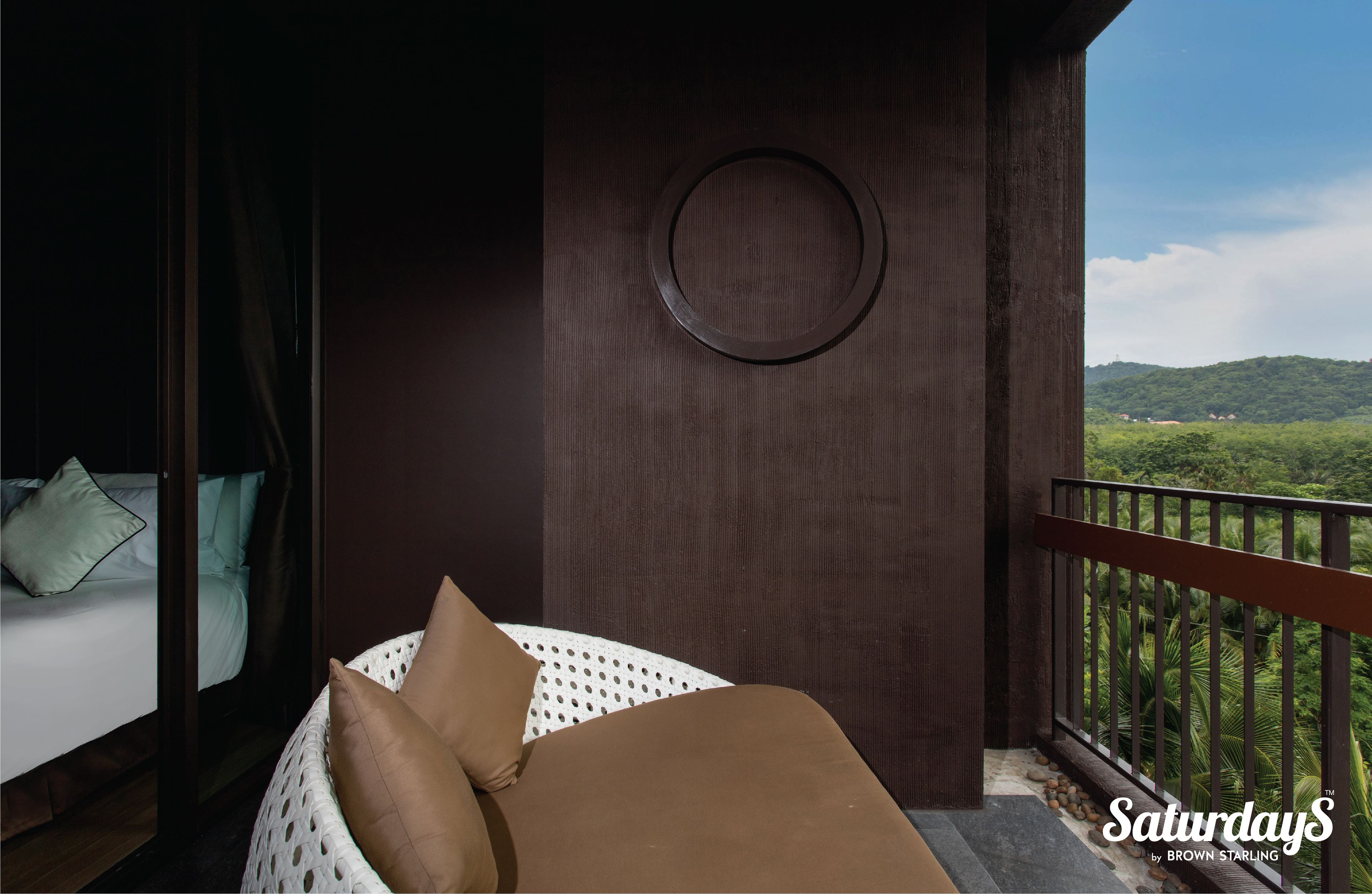 A balcony with a bed, a circular light fixture, and a view of green hills.