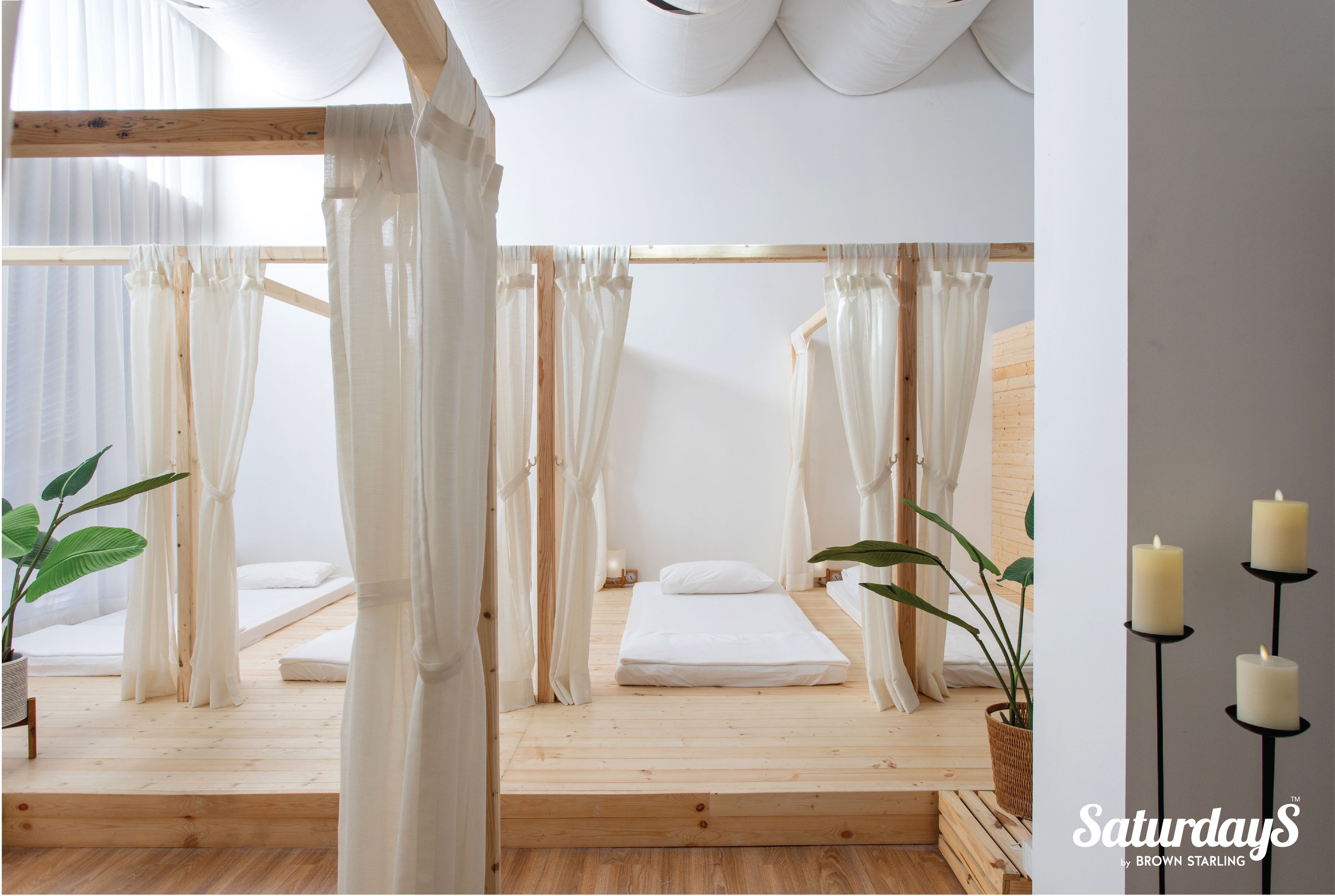 Ein schlicht eingerichtetes Schlafzimmer mit einem hölzernen Plattformbett, transparenten Vorhängen und einer Topfpflanze.