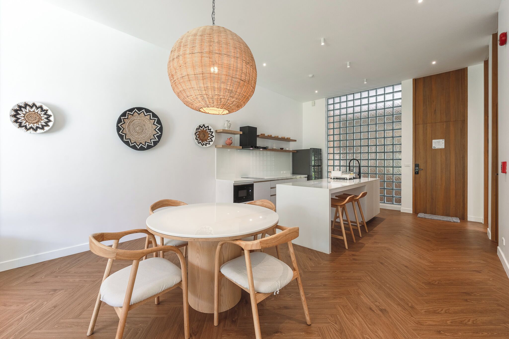 A modern kitchen with a round dining table and chairs, a hanging light fixture, and a glass partition wall.