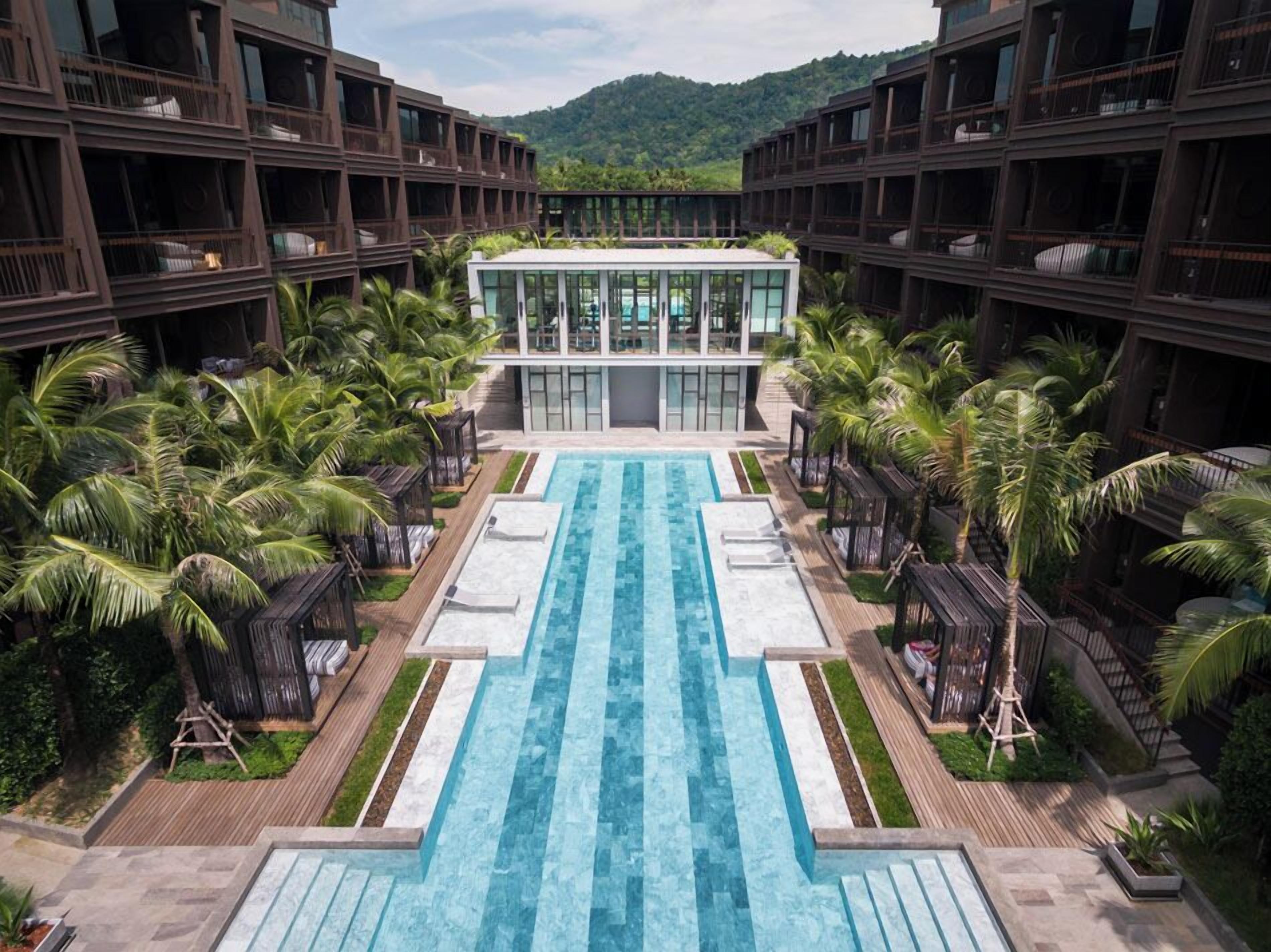 A hotel with a central swimming pool, multiple balconies, and lush greenery.