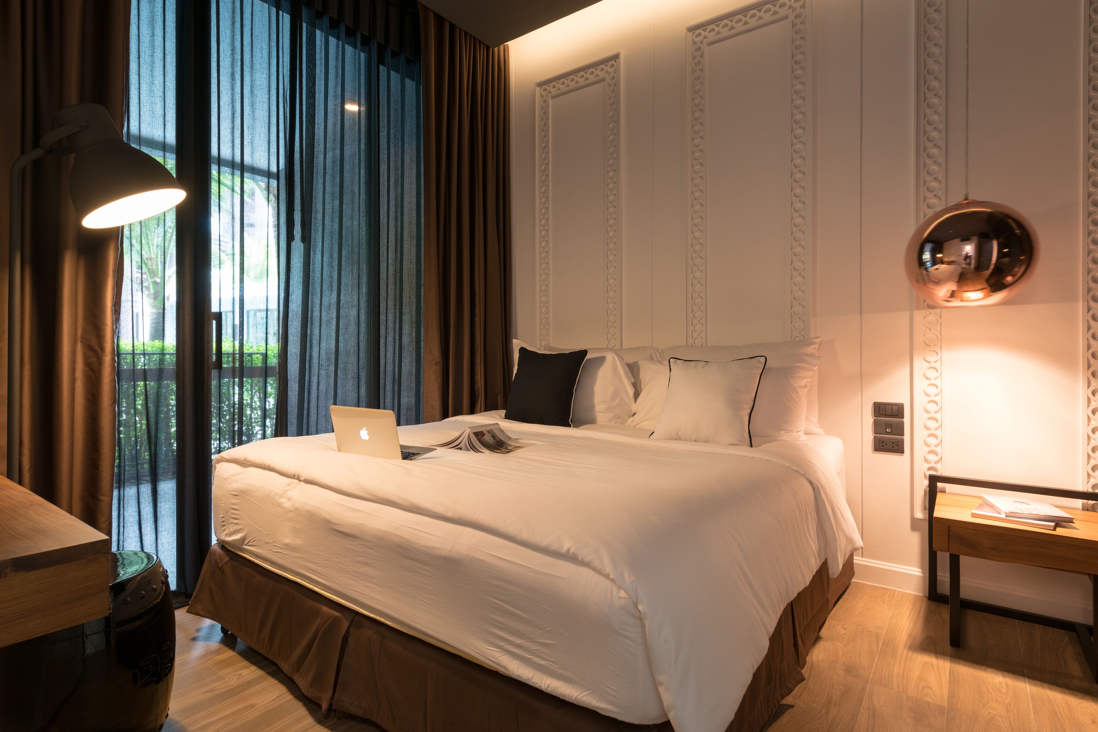 A modern hotel room with a large bed, a desk, and a laptop.