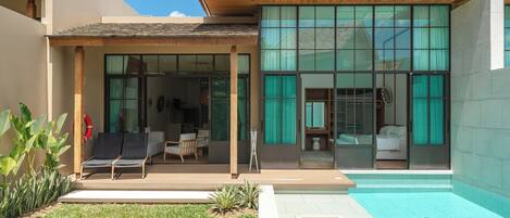 A modern house with a swimming pool, a covered patio, and a large glass door leading to a bedroom.