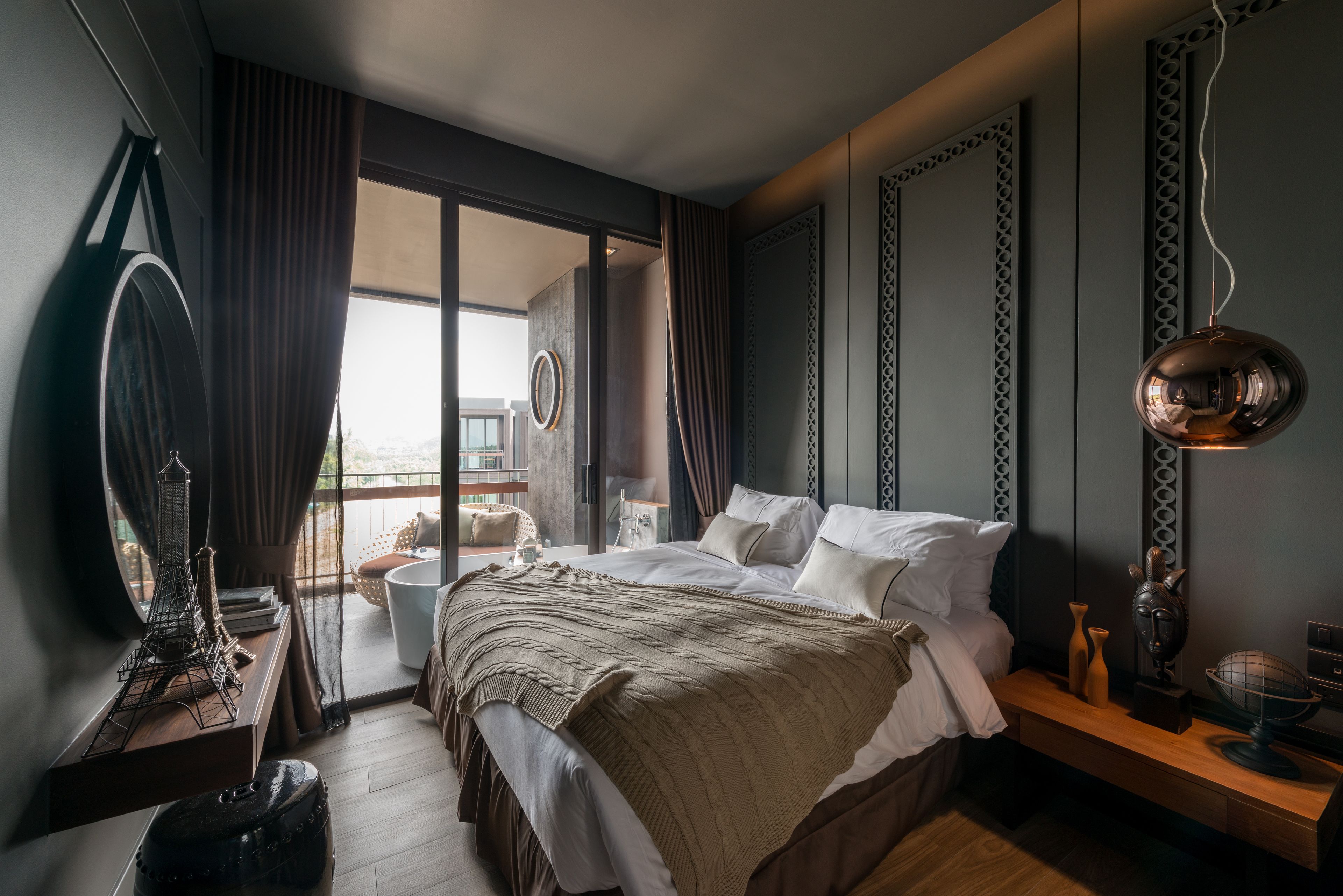 Ein modernes Schlafzimmer mit einem großen Bett, einem kleinen Tisch, einem dekorativen Spiegel und Blick ins Freie.