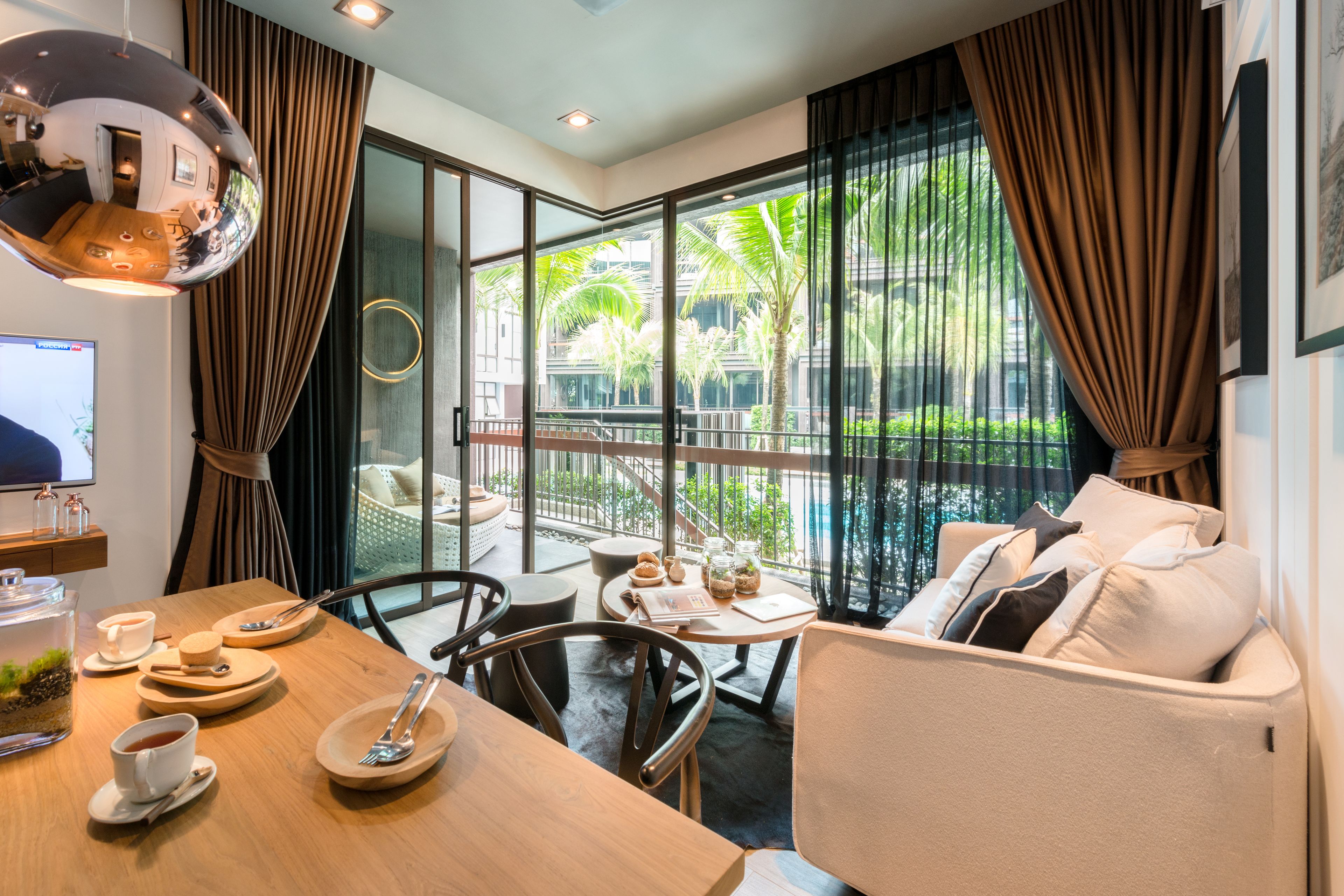 Une chambre d’hôtel moderne dotée d’un coin repas, d’un canapé et d’un balcon offrant une vue sur les palmiers.