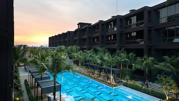 A modern hotel with a large outdoor swimming pool, surrounded by palm trees and a sunset view.