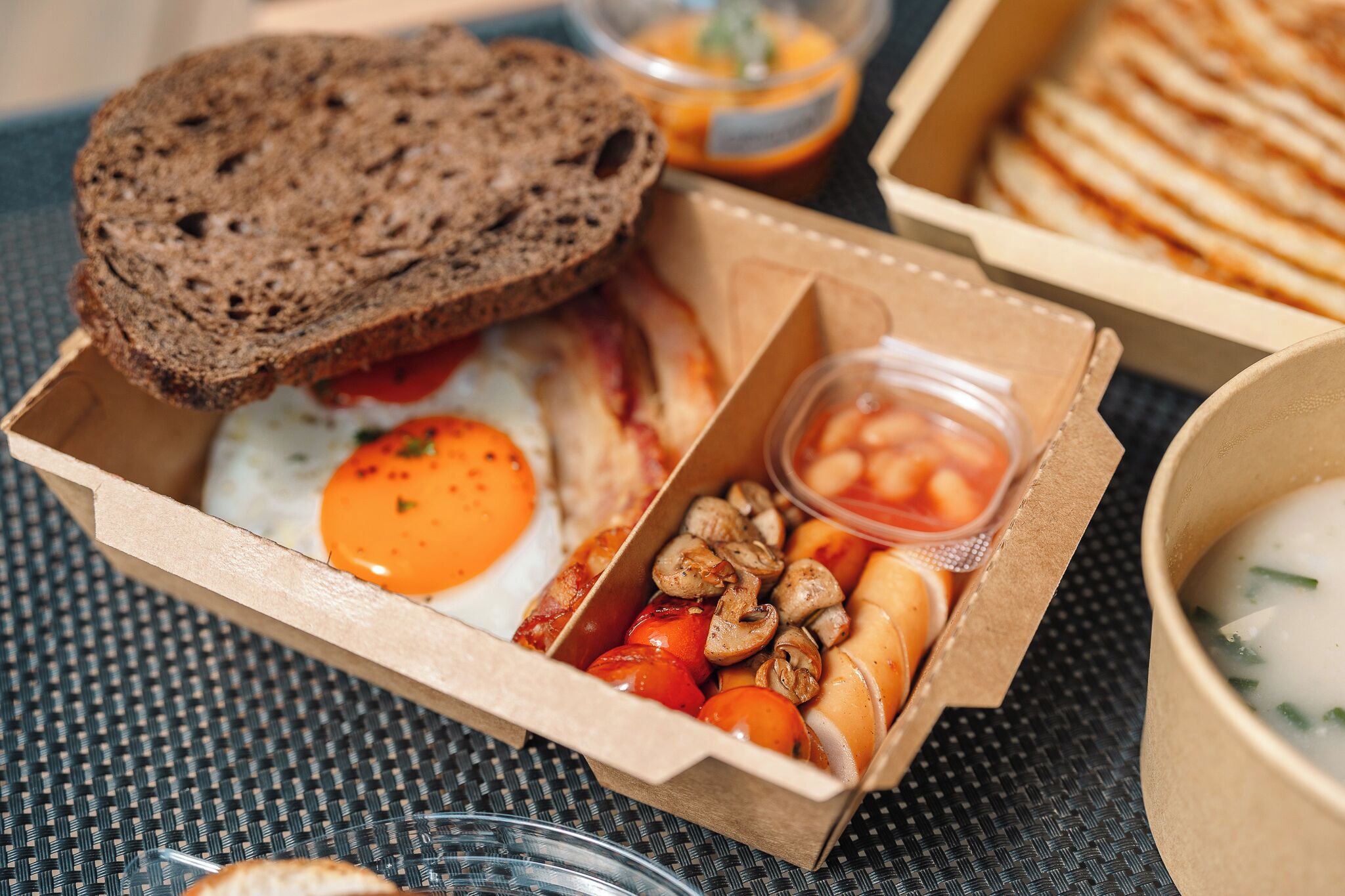 A meal with eggs, mushrooms, tomatoes, and bread in a cardboard box.