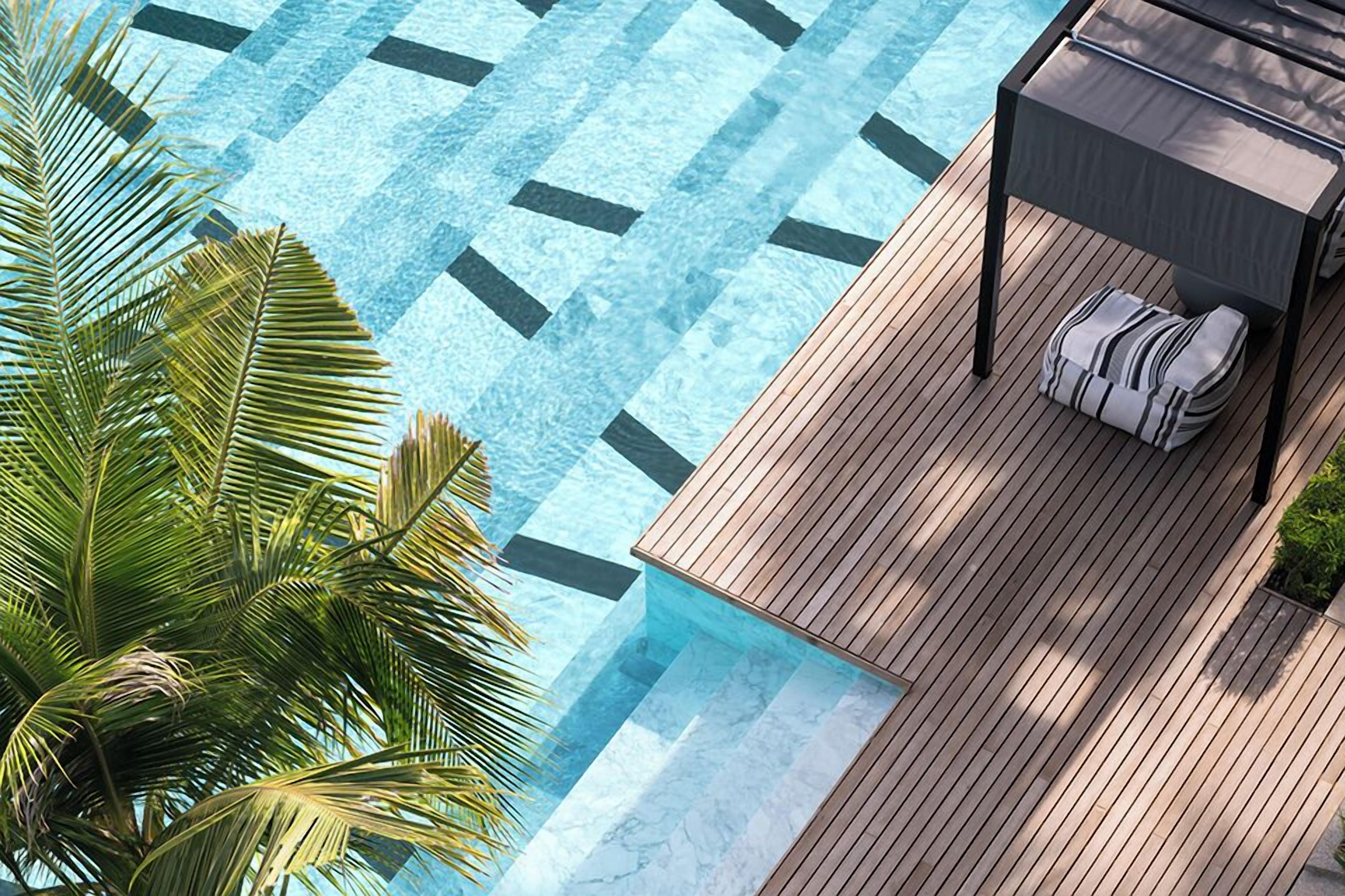 A pool area with a wooden deck, a lounge chair, and a palm tree.