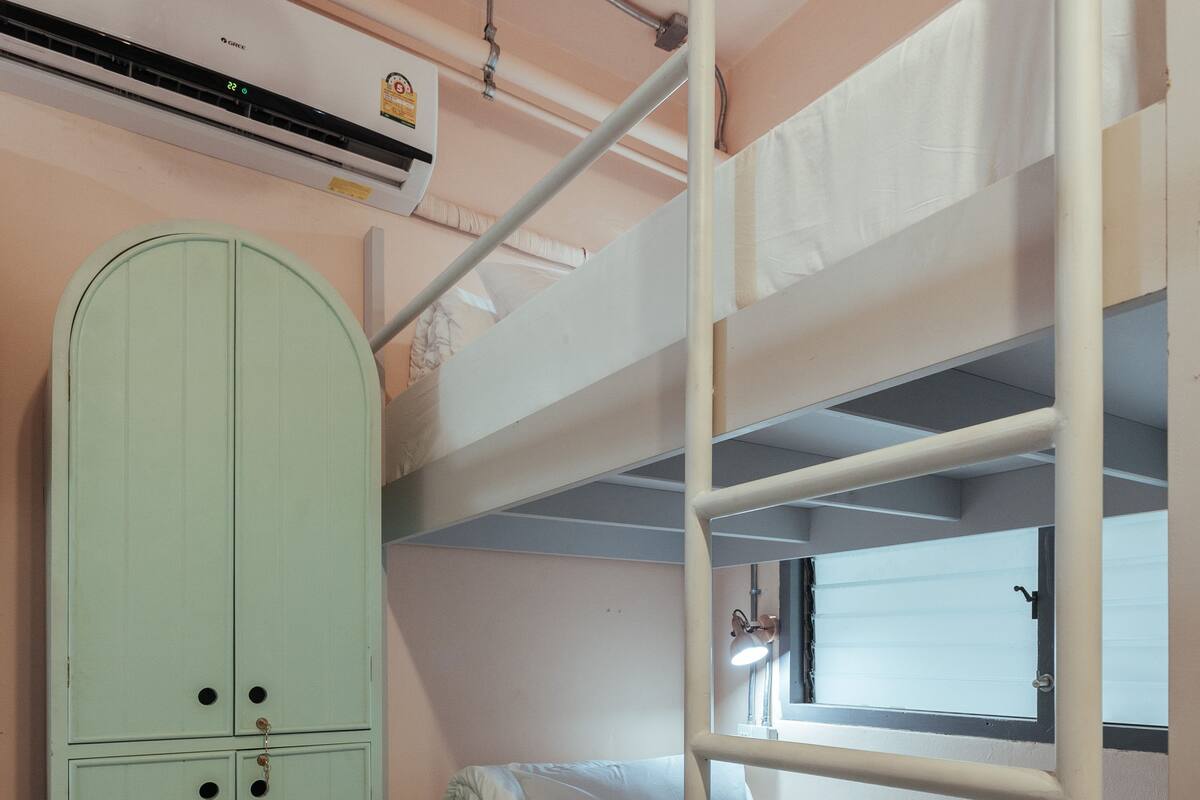 A bunk bed room with a green wardrobe, a window, and an air conditioning unit.