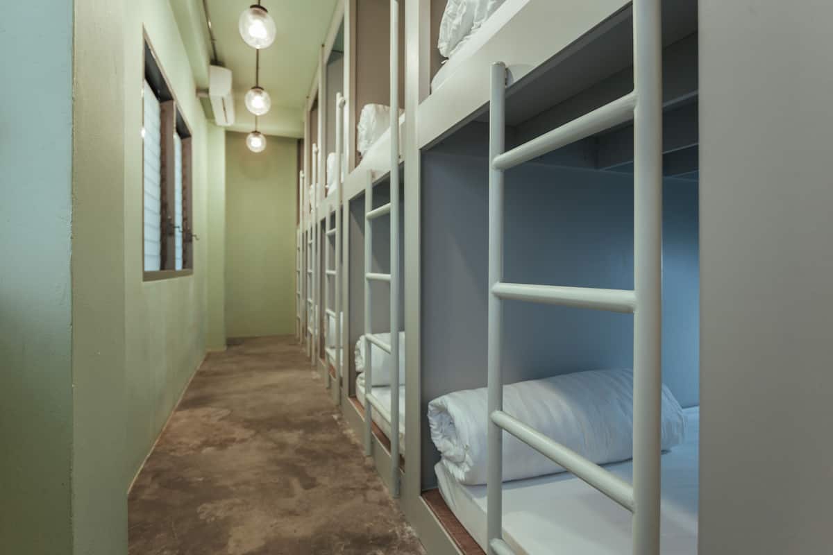 A narrow hallway with bunk beds, each with a mattress and pillows, and a window on the left.