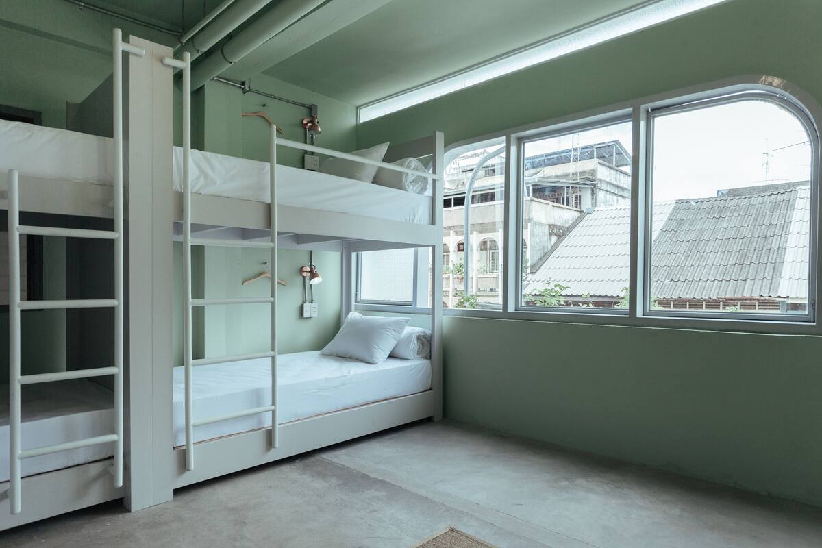 A bunk bed room with a window, a ladder, and a view of buildings outside.